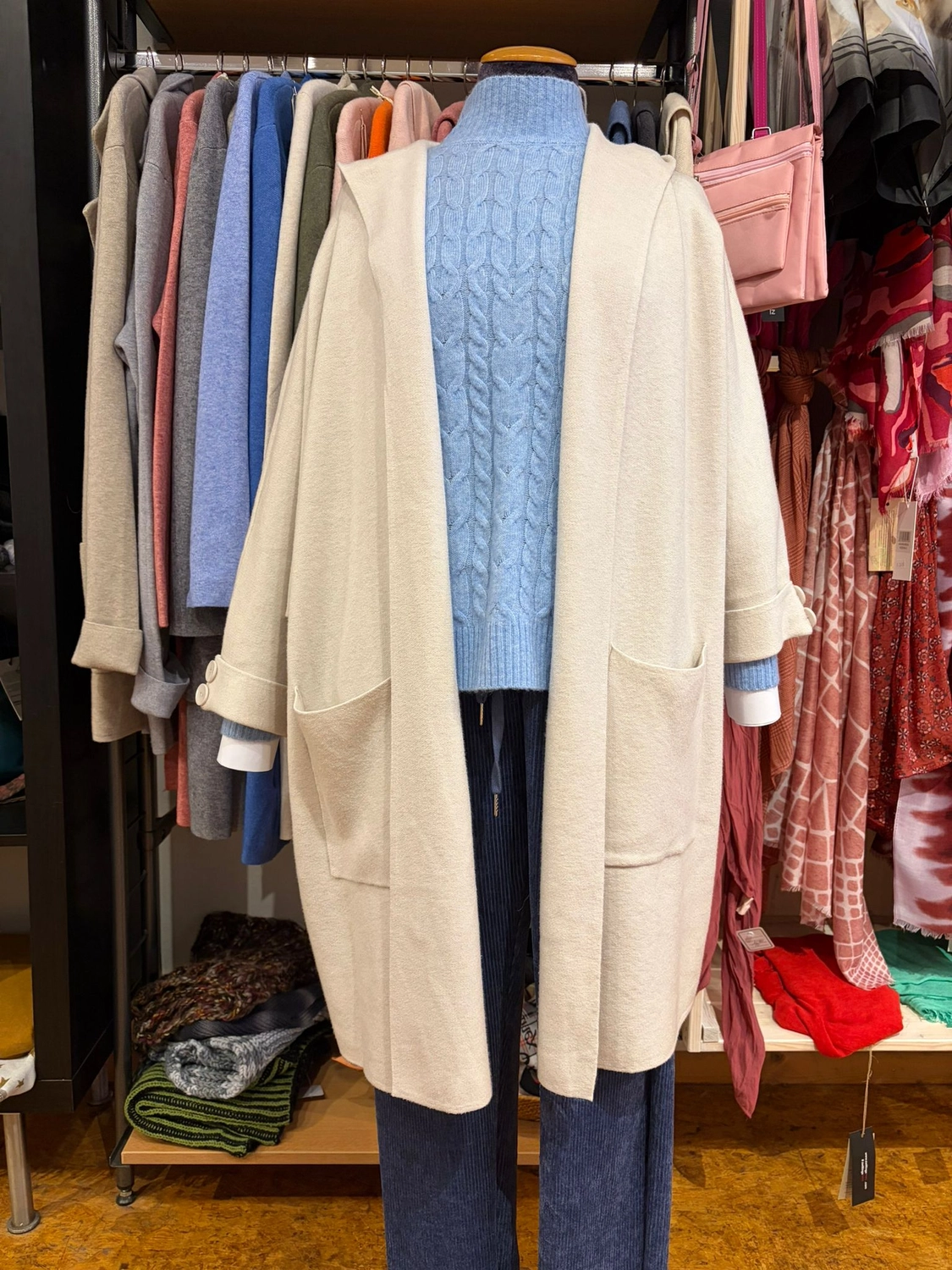 Mode & Handarbeitsdiele - Wolle, Kunsthandwerk, Mode und Accessoires - Eine Schaufensterpuppe mit hellblauem Zopfstrick-Rollkragenpullover und einer langen, cremefarbenen, offenen Strickjacke.