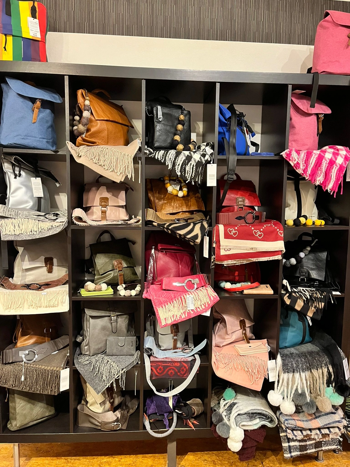 Mode & Handarbeitsdiele - Wolle, Kunsthandwerk, Mode und Accessoires - Ein Verkaufsregal mit verschiedenen farbenfrohen Handtaschen, Rucksäcken und Accessoires.