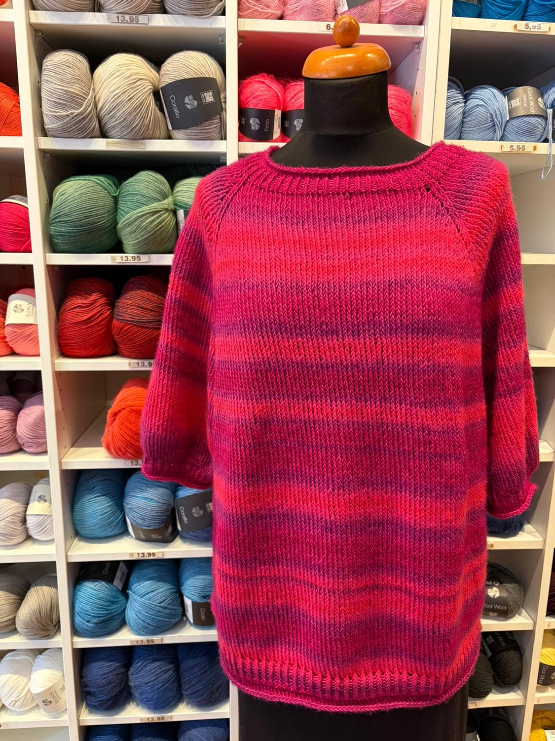 Mode & Handarbeitsdiele - Wolle, Kunsthandwerk, Mode und Accessoires - Gestreifter Pullover: Ein rosa-lila gestreiftes Strickoberteil vor Regalen mit Wolle.