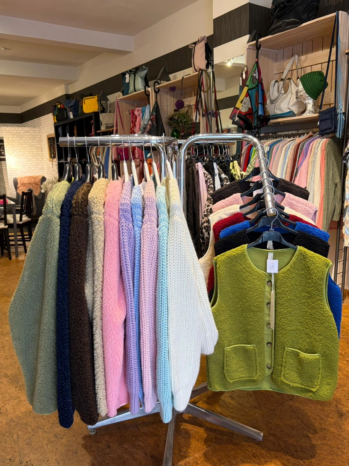 Mode & Handarbeitsdiele - Wolle, Kunsthandwerk, Mode und Accessoires - Ein Kleiderständer in einer Boutique mit farbenfrohen Pullovern und einer leuchtend grünen, strukturierten Weste.