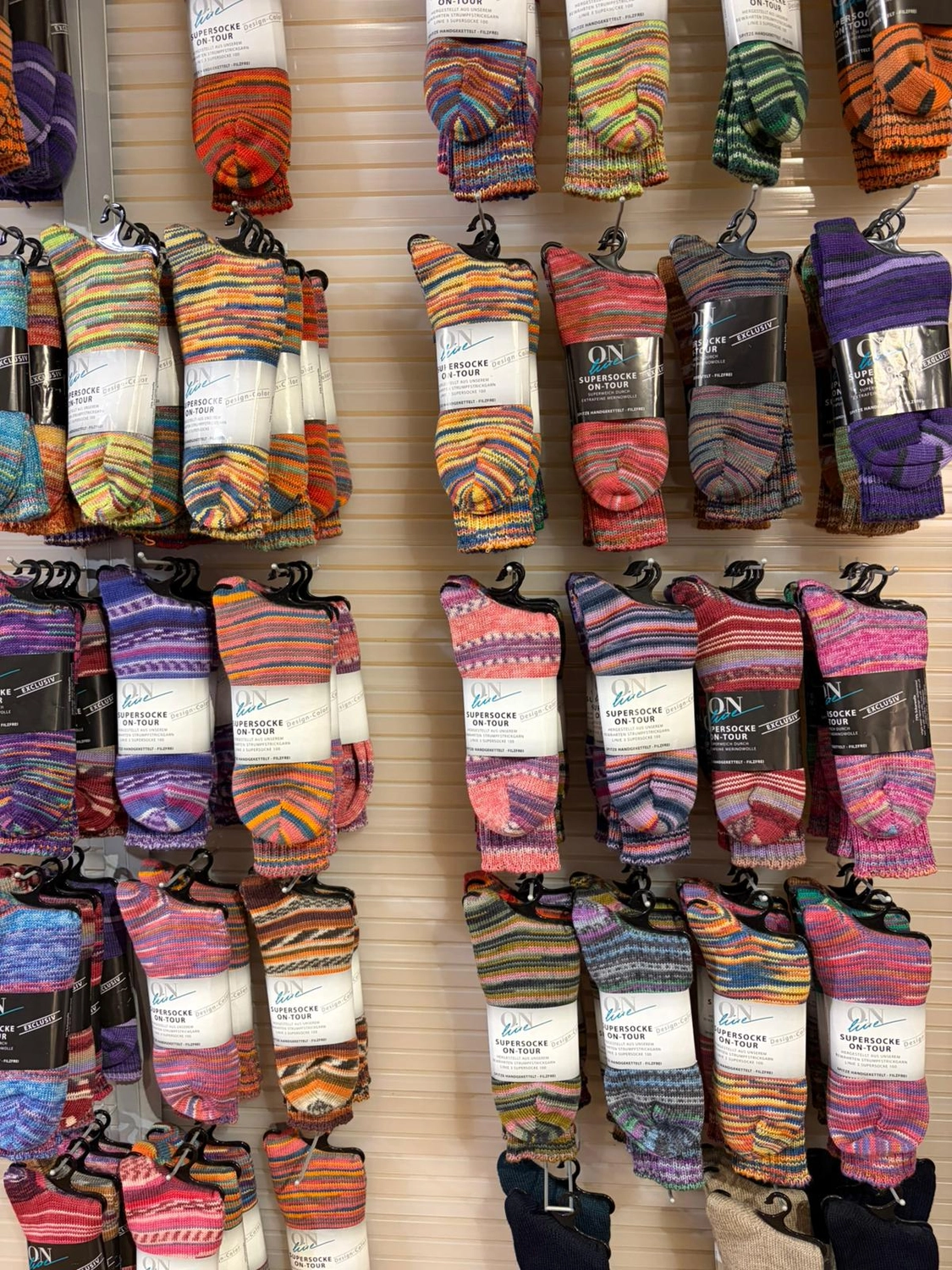Mode & Handarbeitsdiele - Wolle, Kunsthandwerk, Mode und Accessoires - Socken: Eine Wandpräsentation mit zahlreichen Paaren farbenfroher, gemusterter Socken.