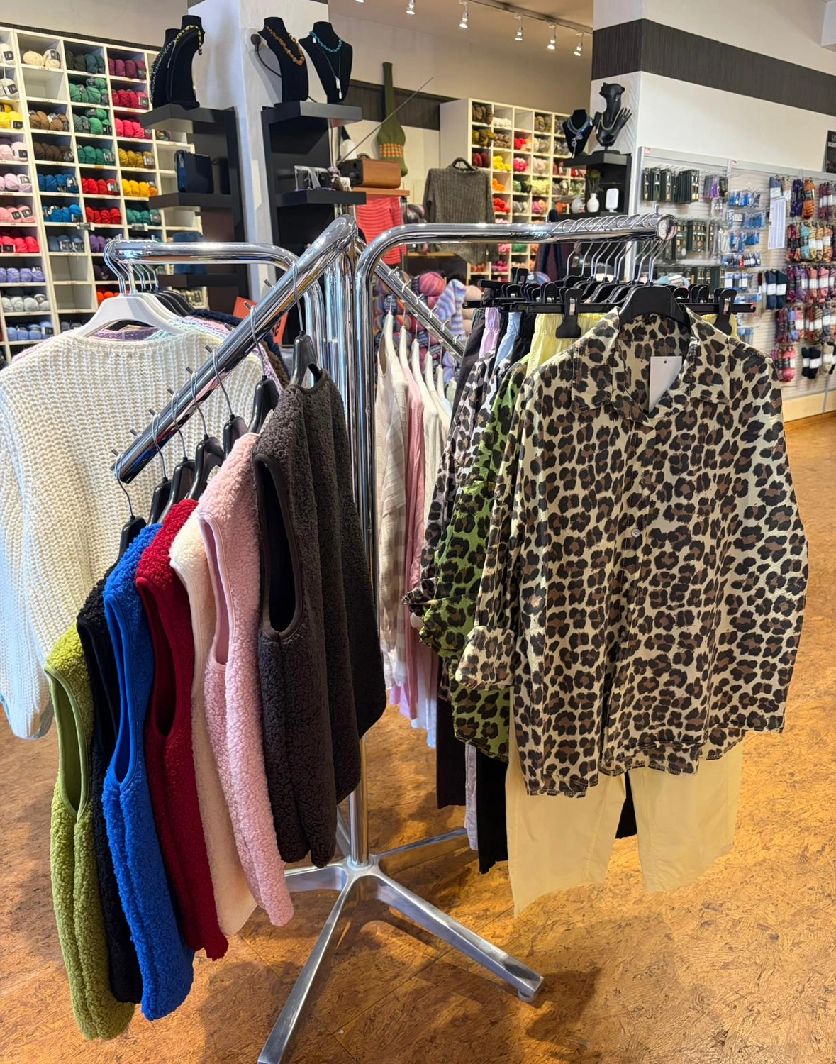 Mode & Handarbeitsdiele - Wolle, Kunsthandwerk, Mode und Accessoires - Ein Kleiderständer mit verschiedenen gemusterten und unifarbenen Kleidungsstücken, darunter ein Leopardenmusterhemd.