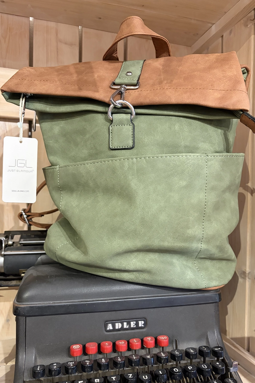 Mode & Handarbeitsdiele - Wolle, Kunsthandwerk, Mode und Accessoires - Ein grüner Canvas-Rucksack mit brauner Klappe, der auf einer alten schwarzen Schreibmaschine steht.