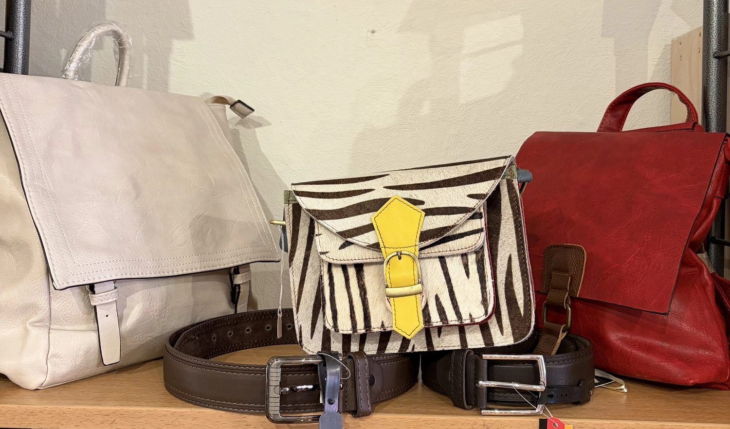 Mode & Handarbeitsdiele - Wolle, Kunsthandwerk, Mode und Accessoires - Eine Kollektion von Modeaccessoires, darunter eine weiße Satchel-Tasche, eine Umhängetasche mit Zebramuster, eine rote Handtasche und mehrere Ledergürtel.