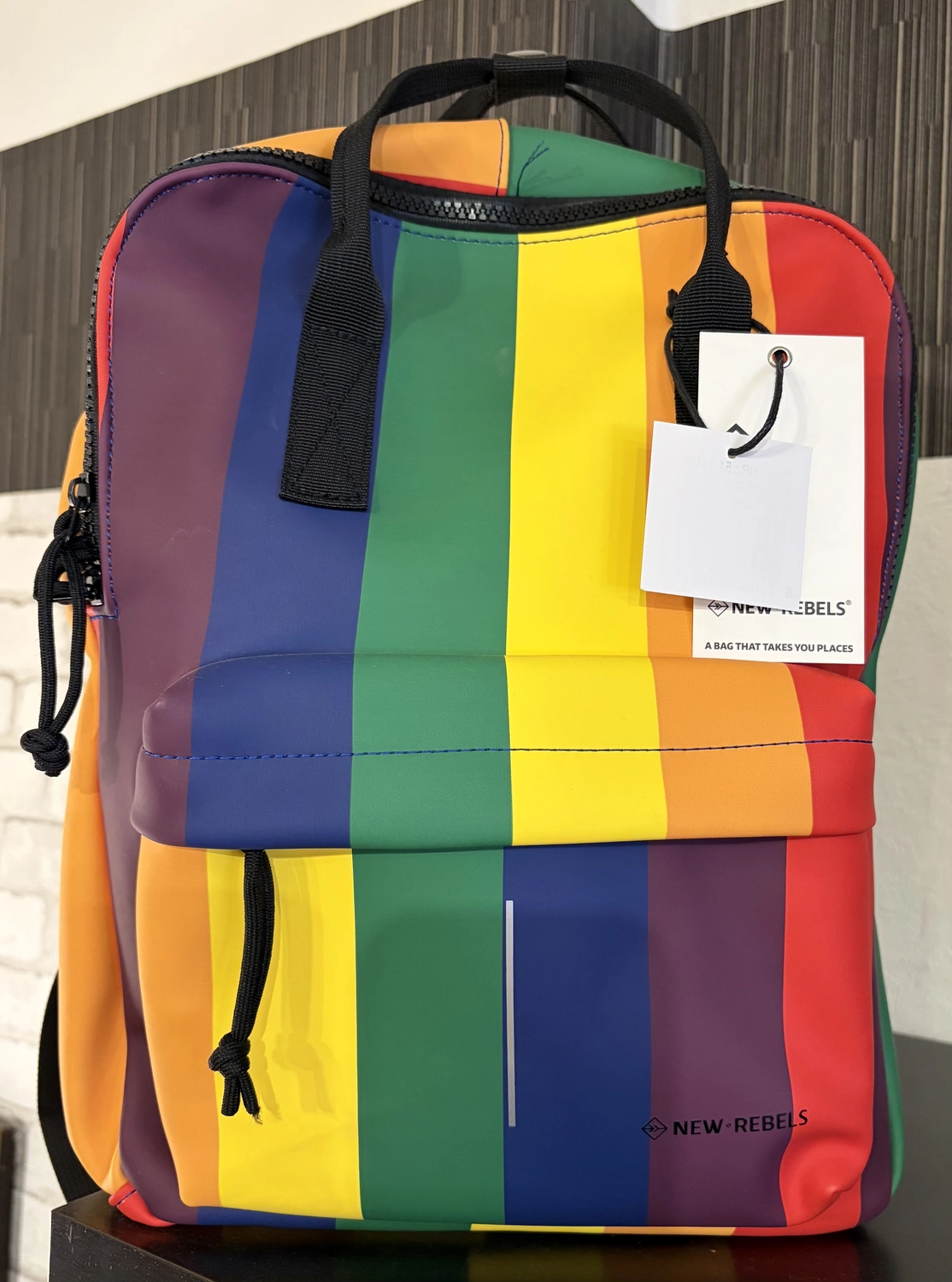 Mode & Handarbeitsdiele - Wolle, Kunsthandwerk, Mode und Accessoires - Ein leuchtend bunter, gestreifter Rucksack mit gelbem Tragegriff und weißem Preisschild.