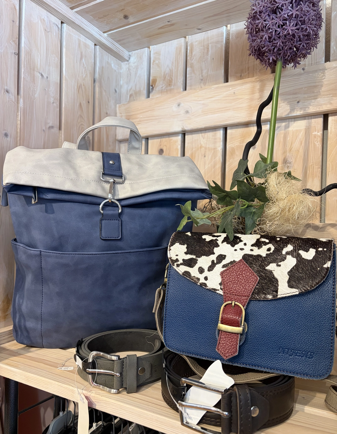 Mode & Handarbeitsdiele - Wolle, Kunsthandwerk, Mode und Accessoires - Ein rustikales Display mit einer blauen Wildledertasche, einer Handtasche mit Kuhfellmuster und mehreren dunklen Ledergürteln.