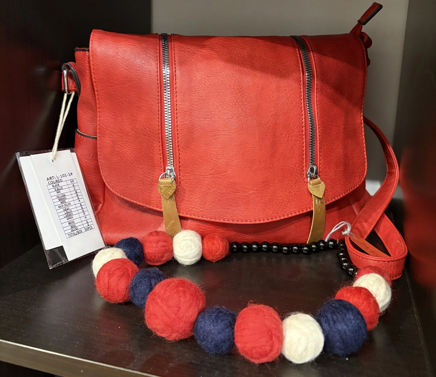 Mode & Handarbeitsdiele - Wolle, Kunsthandwerk, Mode und Accessoires - Eine leuchtend rote Leder-Umhängetasche mit Reißverschlussdetails, kombiniert mit einer auffälligen Filzperlenkette in Rot, Weiß und Marineblau.