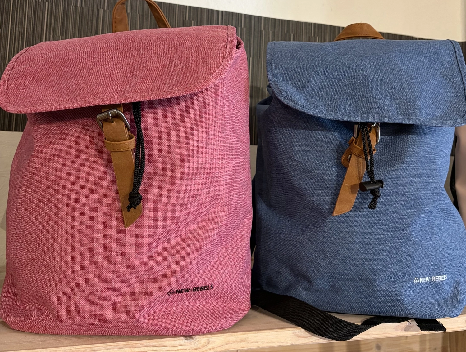 Mode & Handarbeitsdiele - Wolle, Kunsthandwerk, Mode und Accessoires - Zwei Canvas-Rucksäcke mit Überschlag und braunen Riemenverschlüssen, einer in Rosa und einer in Blau.